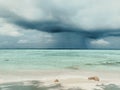 A rain over a calm sea. Maldives, a beach with the white sand near the turquoise ocean. A sky with dark storm clouds. Royalty Free Stock Photo