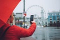 Rain photography. Girl with red umbrella taking photos in the rain. Woman traveler take pictures on rainy day Royalty Free Stock Photo