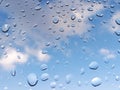 Rain water drops on glass with tropical blue sky background with clouds. Abstract texture of drops of rain on a window glass. Royalty Free Stock Photo