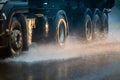 Rain water splash flow from wheels of heavy truck moving fast in daylight city with selective focus. Royalty Free Stock Photo