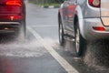 Rain water splash flow from wheels of silver and red cars moving fast in daylight city with selective focus. Royalty Free Stock Photo