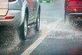 Rain water splash flow from wheels of silver and red cars moving fast in daylight city with selective focus. Royalty Free Stock Photo