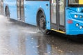 rain water splashes flow from wheels of blue trolleybus moving in daylight city with selective focus