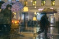 Rain on a window, looking out to people in a night street scene. Silhouettes of people with umbrellas