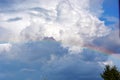 Rainbow in the blue sky above the forest. White clouds float across the sky. Picturesque landscape Royalty Free Stock Photo