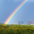 Rainbow in blue sky over city and green trees