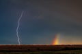 Rainbow and a brilliant lightning bolt streaks across the sky above the field