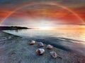 Rainbow at cloudy blue pink sky at sunset sea reflection on water and seashell on beach stones nature landscape