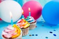 Rainbow color cupcakes with candles on blue background with colorful air balloons, anniversary celebration card Royalty Free Stock Photo