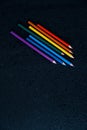 Rainbow color pencils on a black background with drops of water