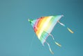Rainbow colored kite flying in clean blue sky. Freedom and summer holiday Royalty Free Stock Photo