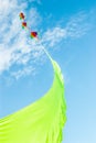 Rainbow colored kites flying high on the end of a vibrant green ribbon against a Summer blue sky and light clouds Royalty Free Stock Photo