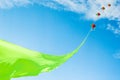 Rainbow colored kites flying high on the end of a vibrant green ribbon against a Summer blue sky and light clouds Royalty Free Stock Photo