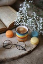 rainbow colored mug of coffee and cookies and glasses and open book and small white blossoms in a wood slice on a table with cloth Royalty Free Stock Photo