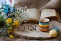 rainbow colored mug of coffee and two cookies and glasses and open book and small flowers in a wood slice on a table Royalty Free Stock Photo