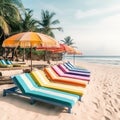 Rainbow colored sunbeds stay in line on sandy summer beach under palms and blue sky. Vacation concept on seascape