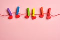 Rainbow colored wooden clothespins with clamped red hearts on pink background Royalty Free Stock Photo