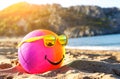 Rainbow colorful smiling beach ball dressed sunglasses on a sandy beach by tsea. Summer holidays concept