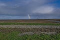 Rainbow with dark blue sky with clouds. grass and stones in foreground. People in the distance. The Netherlands: Waddensea. Unesco Royalty Free Stock Photo