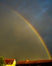 Rainbow in dark sky over sunlit roofs