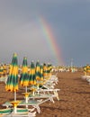 Rainbow emerging from the beach with many closed sunshades after
