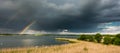 A rainbow emerging from stormy clouds over a pond