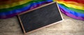 Rainbow flag placed on wooden background. Blackboard in frame with copyspace. 3d illustration