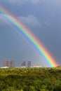 Rainbow in gray sky over city and green trees