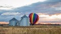 Rainbow hot-air balloon near liftoff by silos on a late summer morning at sunrise Royalty Free Stock Photo