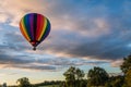 Rainbow hot-air balloon floats over farm field and trees at sunrise Royalty Free Stock Photo