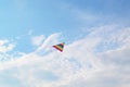 A rainbow kite flying against a blue sky and clouds.