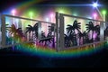 Rainbow lens flare and fence over silhouette of palm trees against light trails Royalty Free Stock Photo