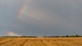 Rainbow over a field on a hot summer stormy day with a dark sky in the background.