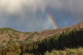 Rainbow over the forest, the phenomenon of nature, rocks and trees, bright colors on the rainbow, rain and cloudy sky Royalty Free Stock Photo