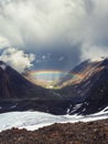 Rainbow over a mountain valley. Gloomy scenery with bright rainbow above glacier in mountain valley. Top view to colorful rainbow Royalty Free Stock Photo