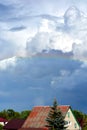 Rainbow over the roofs of houses in the blue sky. White clouds float across the sky. Picturesque landscape Royalty Free Stock Photo