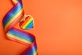 Rainbow ribbon with heart shaped pendant on orange background, top view and space for text. LGBT pride