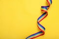 Rainbow ribbon on yellow background, top view with space for text. LGBT pride