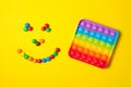 Rainbow silicone sensory antistress pop it toy with smiley from colorful candies on yellow background.