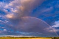 Rainbow Sky Arch on a dramatic stormy sky over yellow fields. A magical natural optical phenomenon that delights