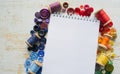 Rainbow spectrum buttons and reels with colorful threads, laid around a notebook with space for text on a light wooden background