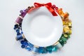 Rainbow spectrum buttons and reels with colorful threads, laid out in form of wreath with red bow around a white plate with space