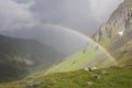 Rainbow stretching over a mountain valley in front of dark thunder storm. Royalty Free Stock Photo