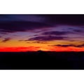 A rainbow of sunset hues contrast the dark silhouette of a lone mountain peak