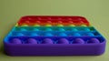 A rainbow toy lies on a yellow background. Blue and Orange Funny Interactive Anti-Stress Silicone Toys. Pop it