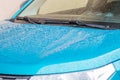 Raindrops on the car. Car element with raindrops close-up. The hood, mirror and glass of a blue car covered in raindrops. Big