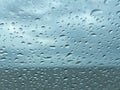 Raindrops on glass with horizon line and clouds in background.