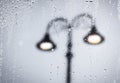 Raindrops running on window glass lit by street lamps. Blurred abstract background Royalty Free Stock Photo