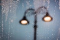 Raindrops running on window glass lit by street lamps. Blurred abstract background Royalty Free Stock Photo