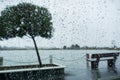 Raindrops on the windshield on a rainy day; bench on the shoreline of a lake in the background